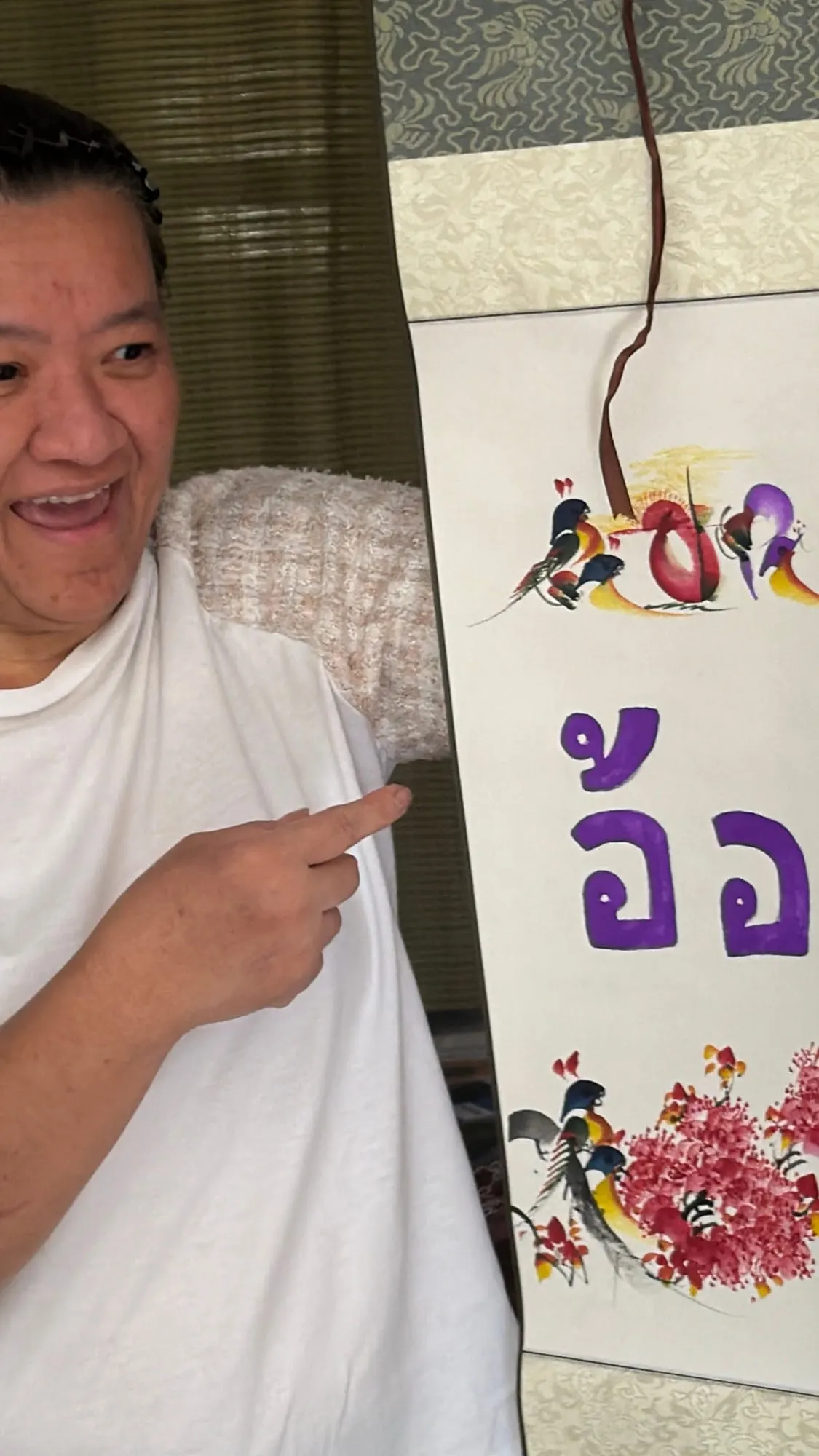 A smiling Wefam family member pointing at hand-painted Thai calligraphy